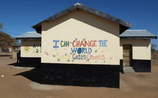 Image of school building against blue sky with colourful handprints and painted letters reading 'I can change the world every child counts'