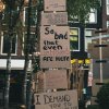 Photo showing series of placards in a stack in what appears to be a square or plaza. The bottom one reads 'I demand you to institutionalise equality'